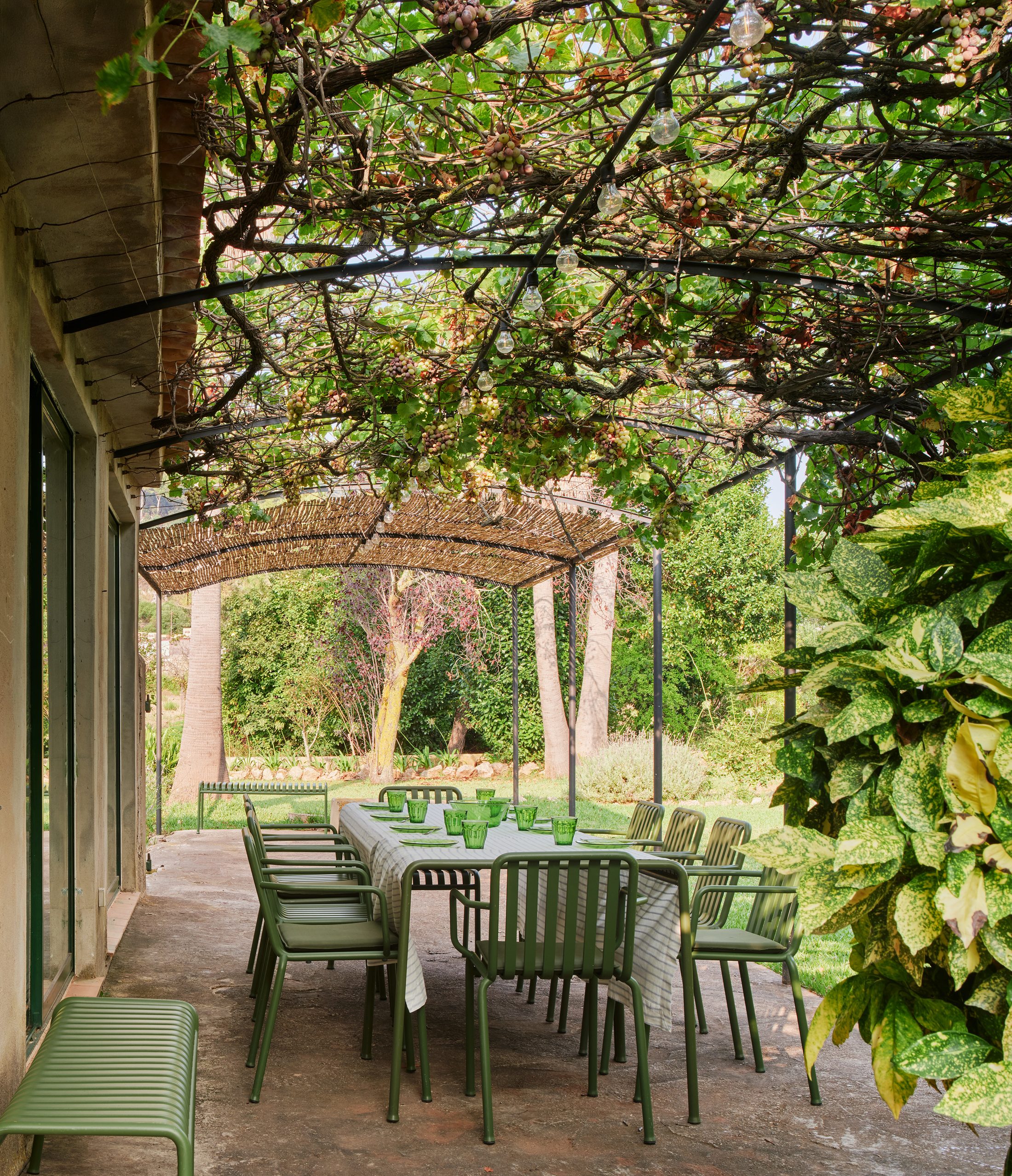 Table set for lunch under the cane pergola of the garden house, looking out over the garden