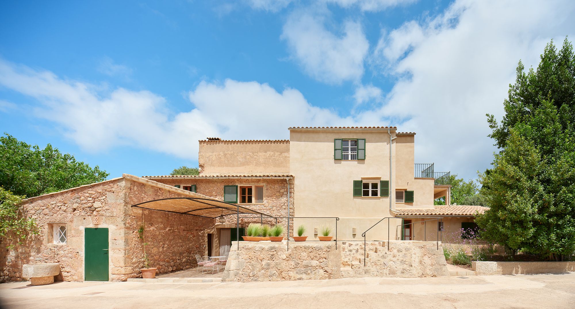 The front of Finca Sa Sinia: stone house with green shutters, the courtyard and the mountain behind