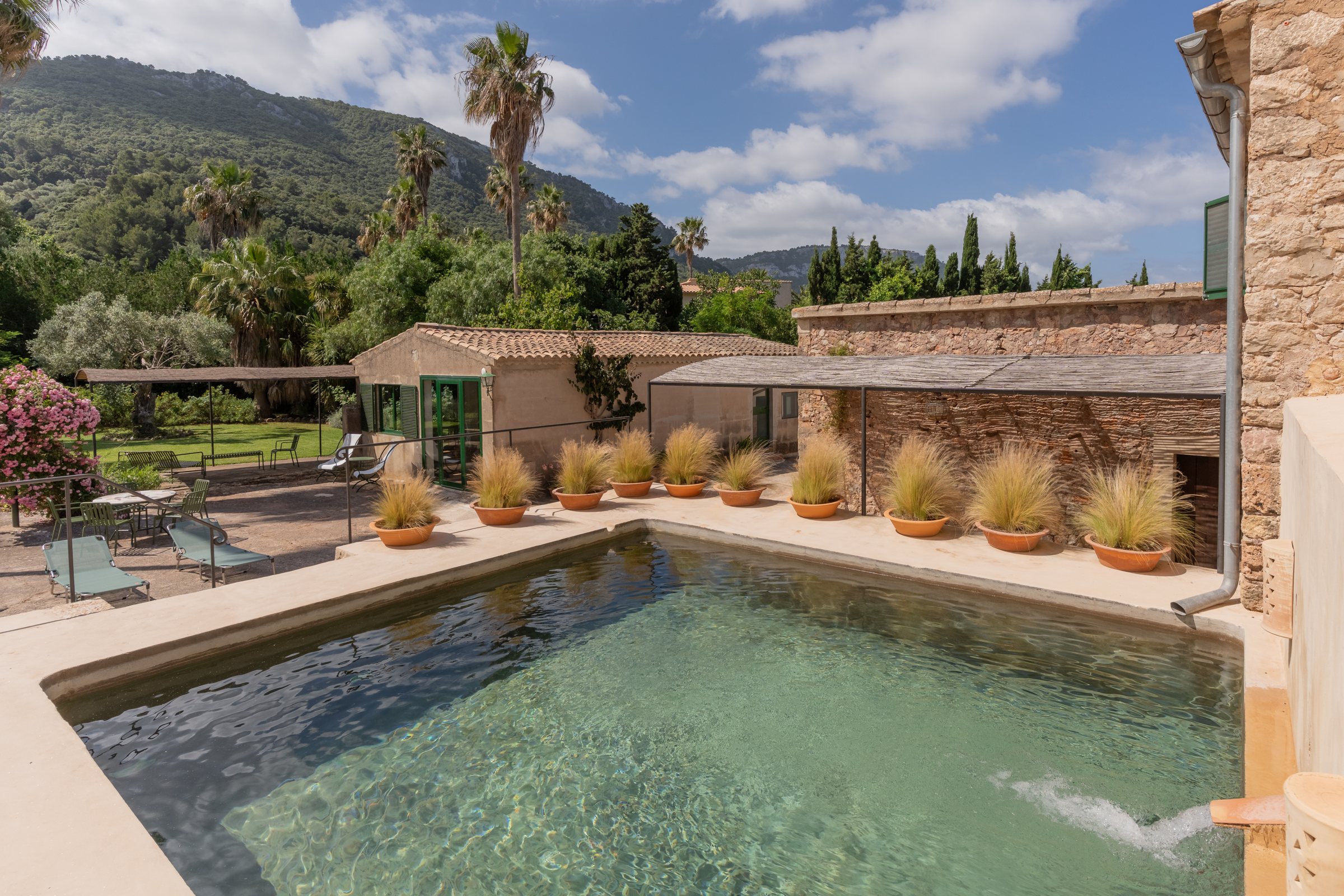 The historic safareig, a traditional Mallorcan water cistern restored and adapted for swimming, beside the stone house, with the Serra de Tramuntana behind