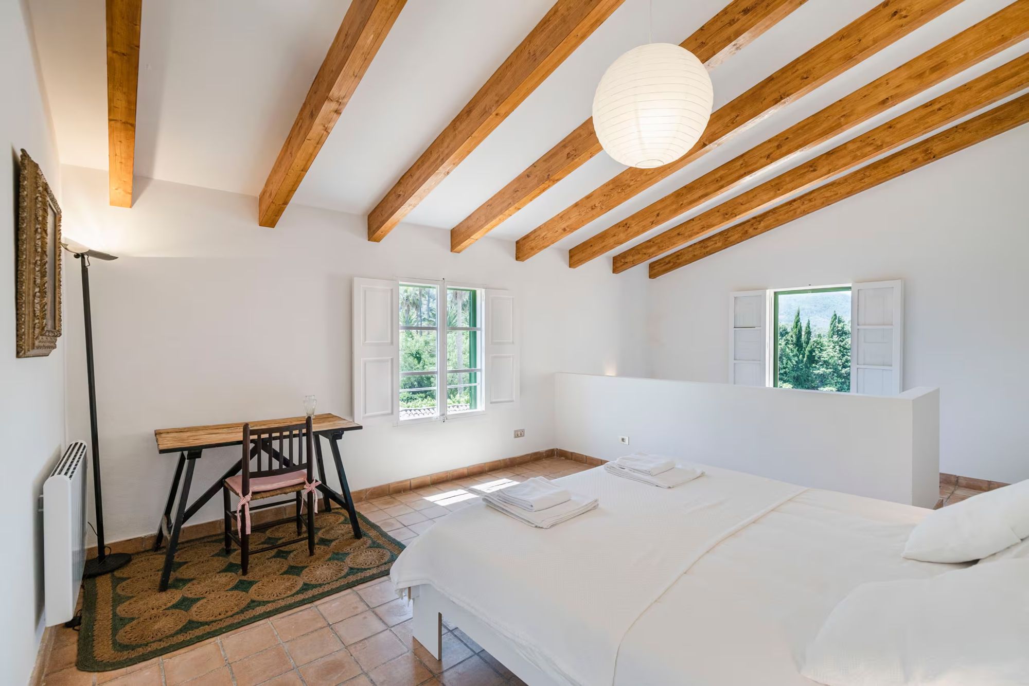 Tía bedroom: king-size bed beneath wooden beams, a desk by the window and a paper lamp